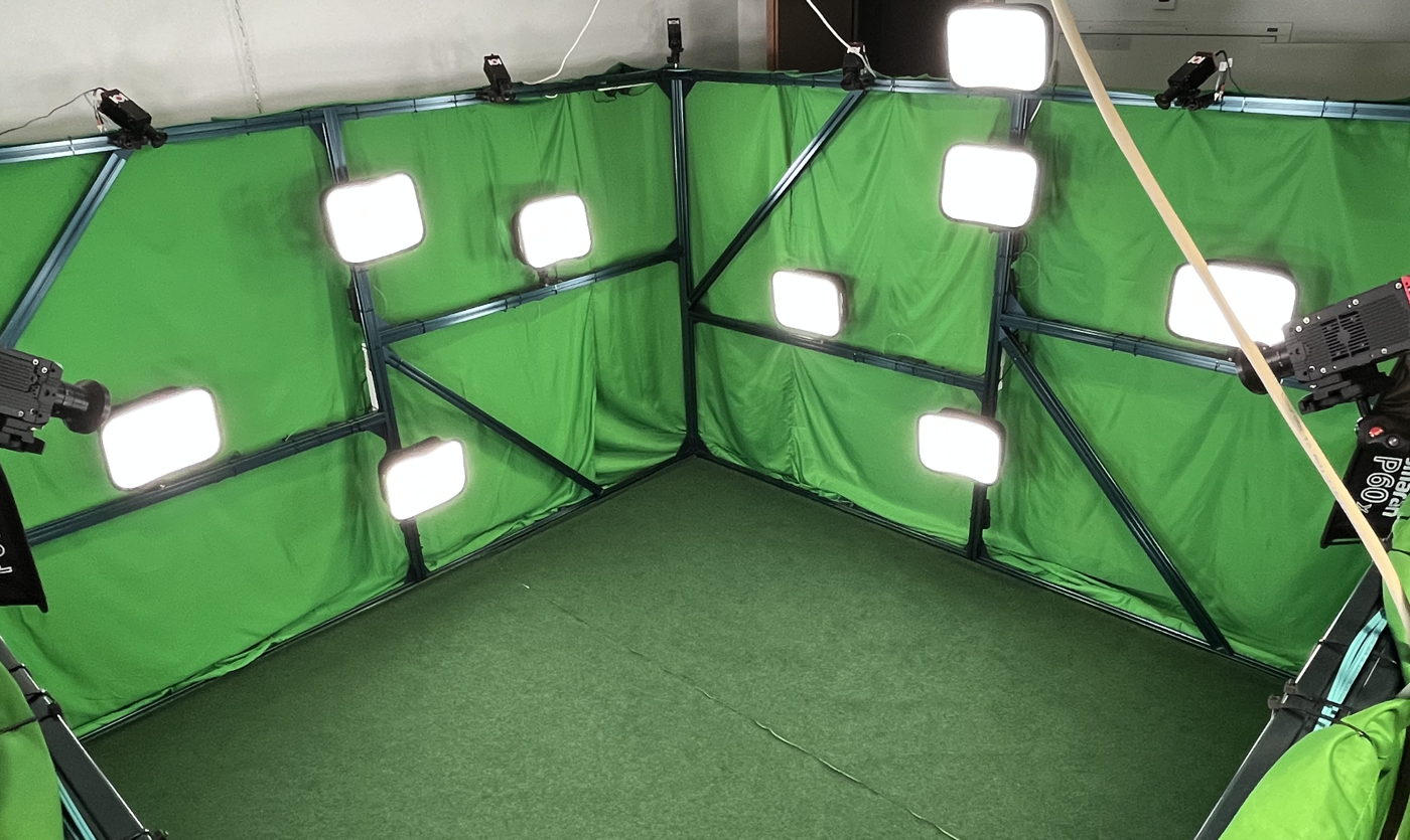 Corner view of the multi-view capture volume, surrounded by mounted cameras, lights and green-screen walls.